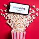 A box of popcorn on its side with popcorn and a phone reading "prime video" spilling out of it.
